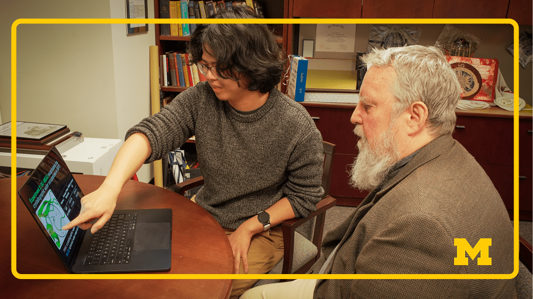 A professor and student collaborate in front of a computer